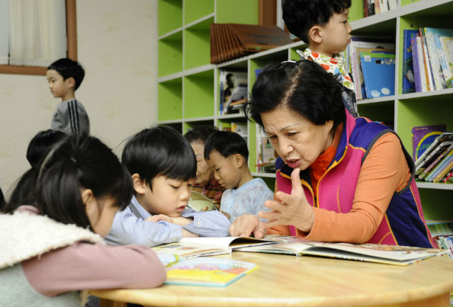 광진구 중곡2동에 위치한 한마음경로당 어린이 북카페에서 어르신이 어린이들에게 동화책을 읽어주고 있는 모습