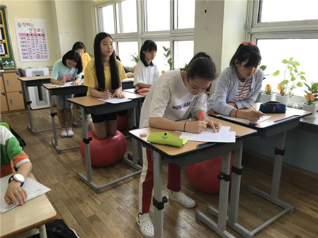 초등학교 학생들이 교실에서 높이 조절 책상과 짐볼을 사용해 서서 공부하고 있다
